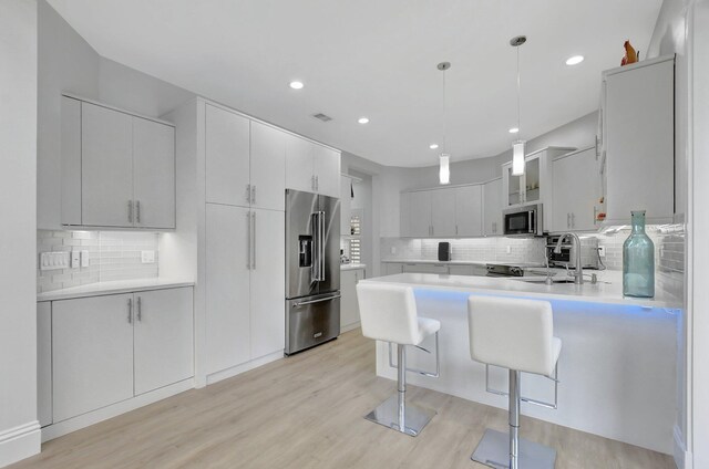 kitchen with white cabinetry, stainless steel appliances, decorative light fixtures, decorative backsplash, and light wood-type flooring