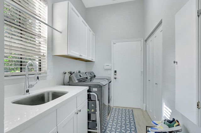 clothes washing area with cabinets, independent washer and dryer, light hardwood / wood-style flooring, and sink