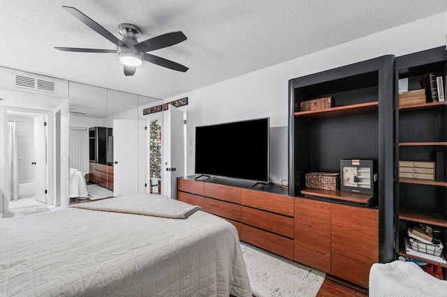 bedroom with ceiling fan, hardwood / wood-style floors, ensuite bathroom, and a textured ceiling