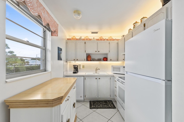 kitchen with white cabinetry, sink, light tile patterned floors, and white appliances