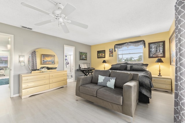 bedroom with a textured ceiling, light hardwood / wood-style flooring, ensuite bath, and ceiling fan