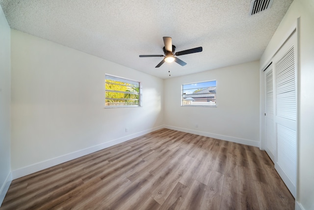 unfurnished bedroom with wood-type flooring, a textured ceiling, a closet, and ceiling fan