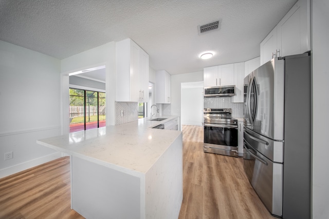 kitchen featuring light wood-type flooring, stainless steel appliances, white cabinetry, and tasteful backsplash