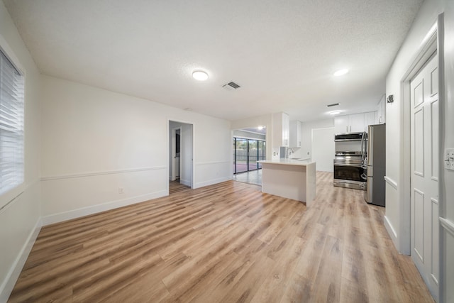 interior space with a textured ceiling, light wood-type flooring, stainless steel appliances, and white cabinetry