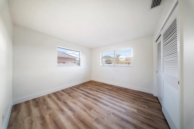 unfurnished bedroom with wood-type flooring, a textured ceiling, a closet, and multiple windows