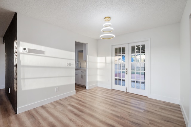 empty room featuring french doors, a textured ceiling, light hardwood / wood-style flooring, and sink