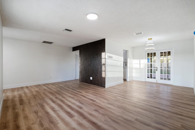 unfurnished living room featuring french doors, light hardwood / wood-style floors, and a textured ceiling