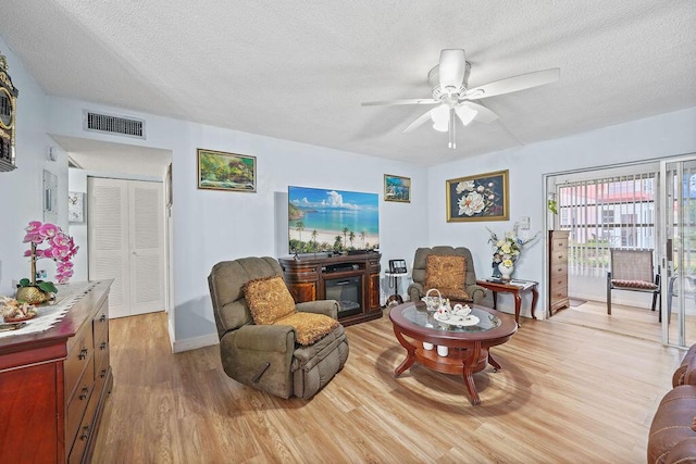 living room with ceiling fan, light hardwood / wood-style floors, and a textured ceiling