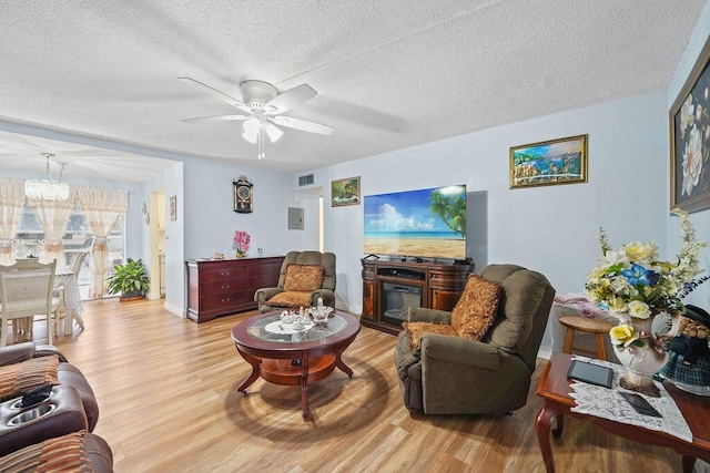 living room featuring a fireplace, ceiling fan with notable chandelier, a textured ceiling, and light wood-type flooring