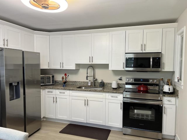 kitchen with dark stone counters, stainless steel appliances, sink, light hardwood / wood-style flooring, and white cabinets