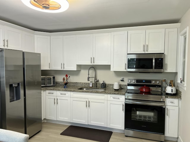 kitchen with white cabinetry, sink, stainless steel appliances, dark stone countertops, and light hardwood / wood-style floors