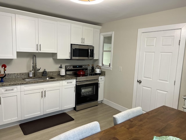 kitchen with appliances with stainless steel finishes, light wood-type flooring, dark stone counters, sink, and white cabinets