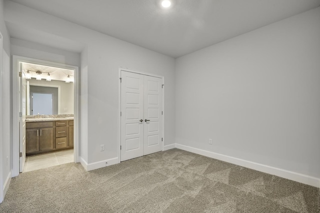 unfurnished bedroom with a closet, sink, light carpet, and ensuite bath