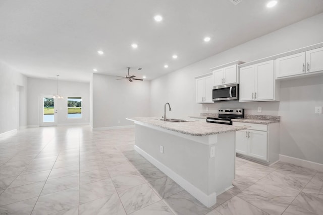 kitchen with appliances with stainless steel finishes, ceiling fan, a kitchen island with sink, sink, and white cabinetry