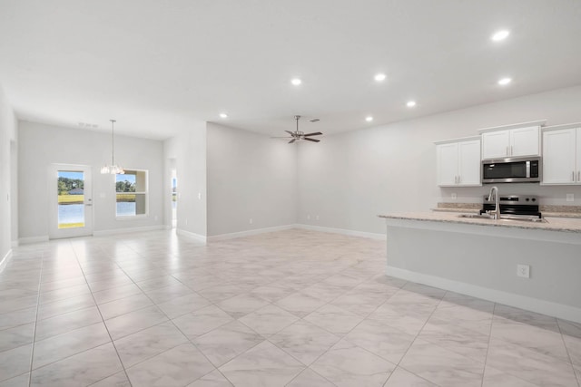 kitchen featuring appliances with stainless steel finishes, light stone counters, ceiling fan with notable chandelier, sink, and white cabinetry