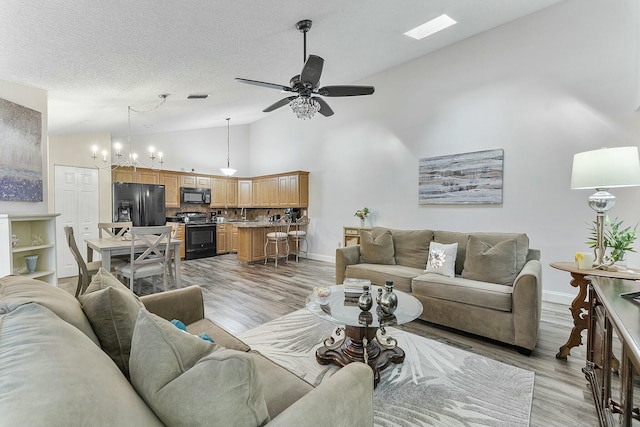 living room featuring a textured ceiling, ceiling fan with notable chandelier, light hardwood / wood-style floors, and high vaulted ceiling