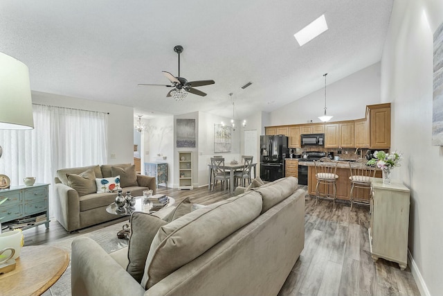 living room with a textured ceiling, ceiling fan with notable chandelier, light hardwood / wood-style floors, and high vaulted ceiling