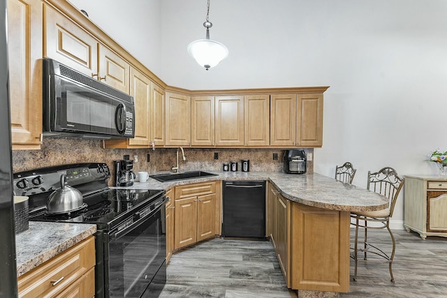 kitchen with sink, kitchen peninsula, decorative light fixtures, a breakfast bar area, and black appliances