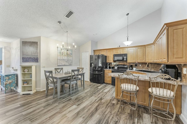 kitchen featuring light stone countertops, decorative backsplash, light wood-type flooring, sink, and black appliances