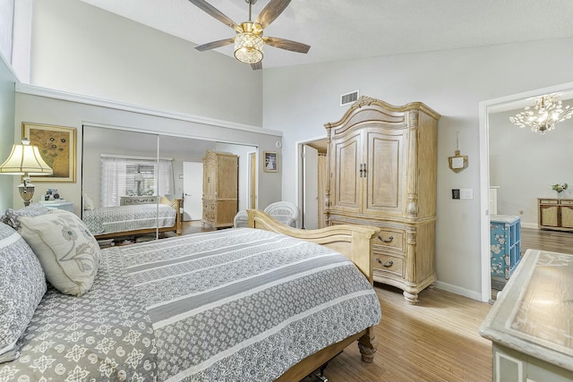 bedroom with a closet, high vaulted ceiling, ceiling fan with notable chandelier, and light wood-type flooring