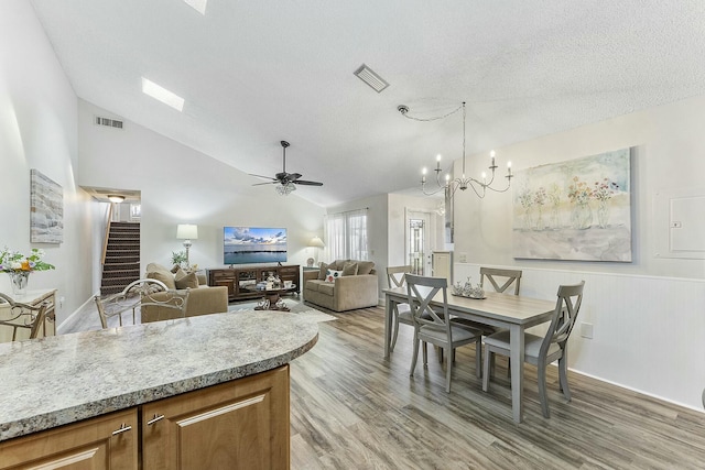 dining area featuring a textured ceiling, ceiling fan with notable chandelier, light hardwood / wood-style flooring, and lofted ceiling