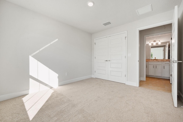 unfurnished bedroom featuring connected bathroom, light colored carpet, a closet, and sink