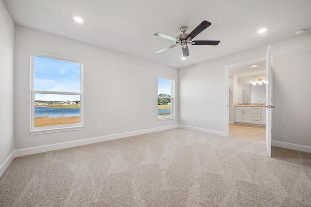 unfurnished bedroom featuring ensuite bath, ceiling fan, a water view, and light carpet