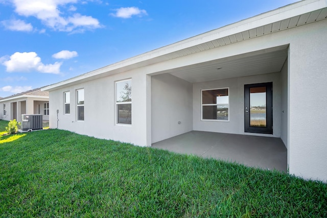 rear view of property featuring stucco siding, a lawn, central AC, and a patio area