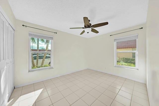 empty room featuring ceiling fan, light tile patterned floors, and a textured ceiling