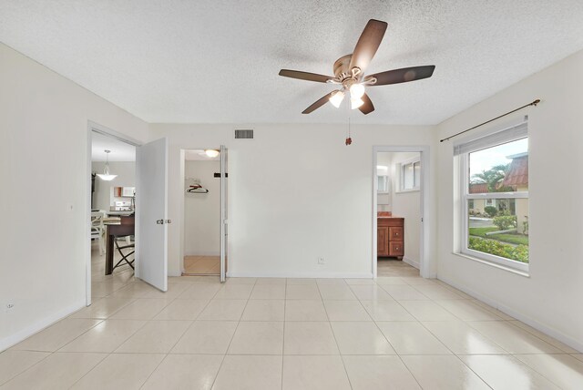 empty room featuring ceiling fan, light tile patterned flooring, and a textured ceiling