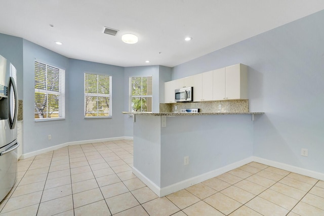 kitchen featuring kitchen peninsula, white cabinetry, light stone counters, and appliances with stainless steel finishes