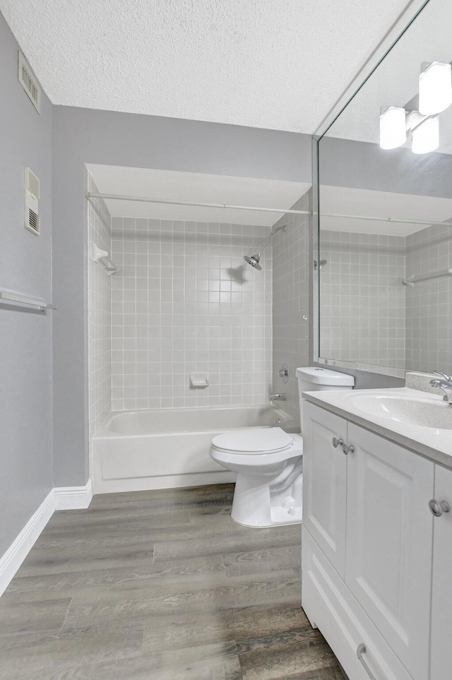 full bathroom with hardwood / wood-style floors, a textured ceiling, toilet, vanity, and tiled shower / bath