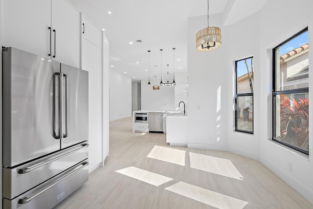 kitchen featuring white cabinetry, sink, hanging light fixtures, a chandelier, and appliances with stainless steel finishes