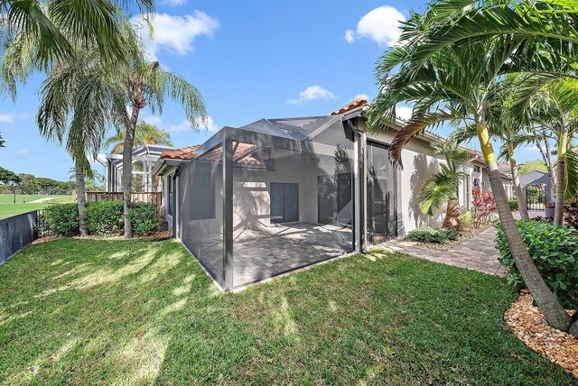 back of house with a yard, glass enclosure, and a patio area