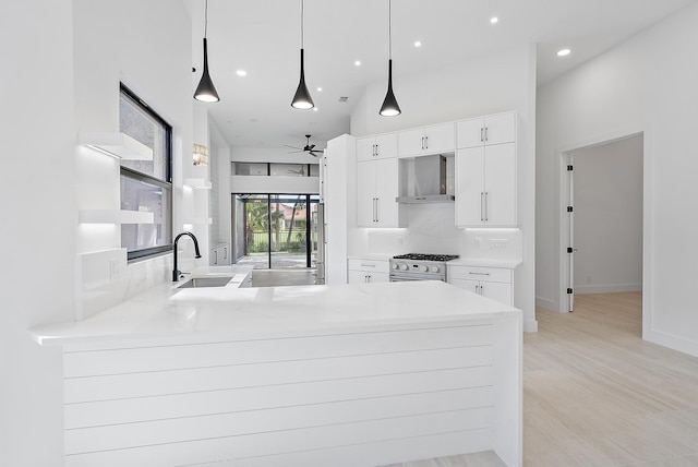 kitchen with pendant lighting, kitchen peninsula, sink, wall chimney exhaust hood, and white cabinetry