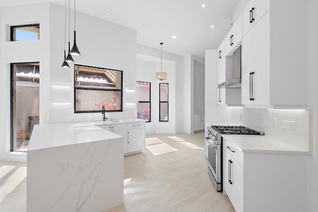 kitchen with white cabinetry, stainless steel range, sink, light stone counters, and decorative light fixtures