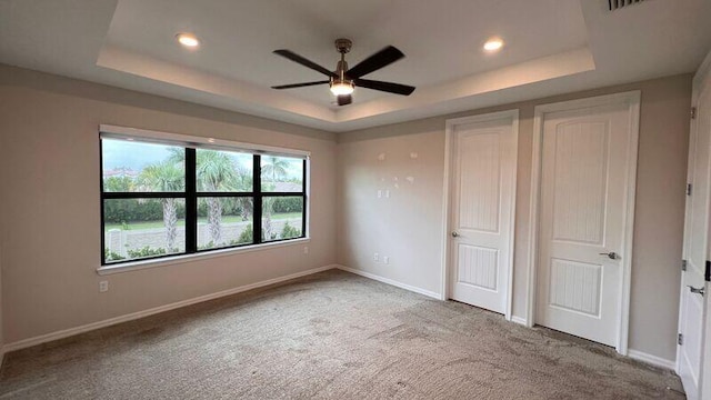 unfurnished bedroom featuring ceiling fan, a raised ceiling, and carpet floors