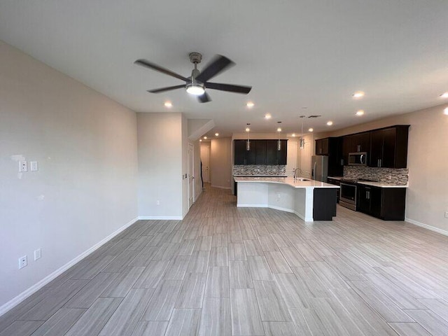 kitchen featuring light wood-type flooring, stainless steel appliances, a kitchen island with sink, and backsplash