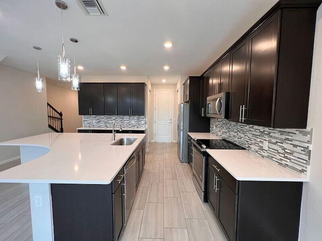 kitchen with appliances with stainless steel finishes, tasteful backsplash, sink, hanging light fixtures, and an island with sink