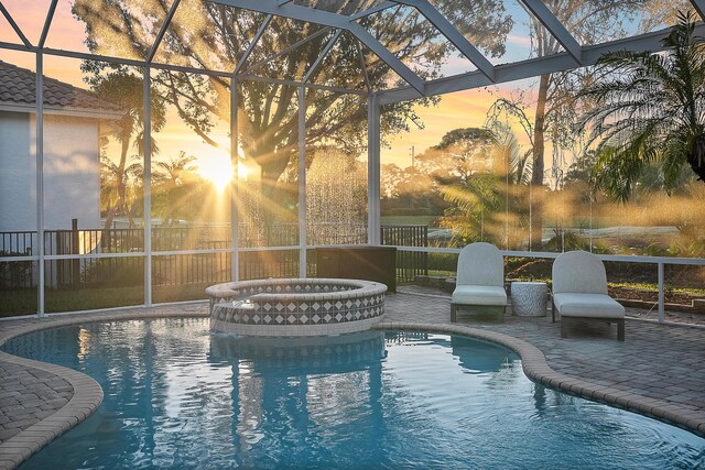 pool at dusk with an in ground hot tub, glass enclosure, and a patio