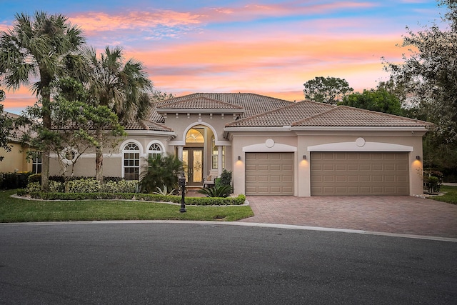 mediterranean / spanish-style home with driveway, an attached garage, stucco siding, french doors, and a tiled roof