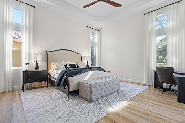 bedroom featuring a raised ceiling, ceiling fan, and light hardwood / wood-style floors