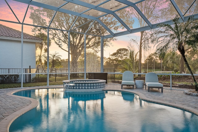 pool at dusk with an in ground hot tub, glass enclosure, and a patio area