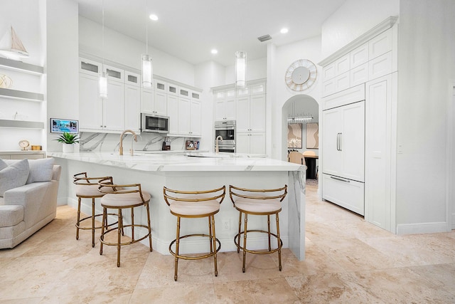 kitchen featuring light stone countertops, appliances with stainless steel finishes, white cabinetry, decorative light fixtures, and a breakfast bar