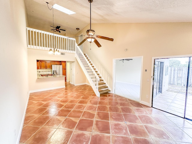 interior space featuring a textured ceiling, high vaulted ceiling, a skylight, light tile patterned flooring, and ceiling fan