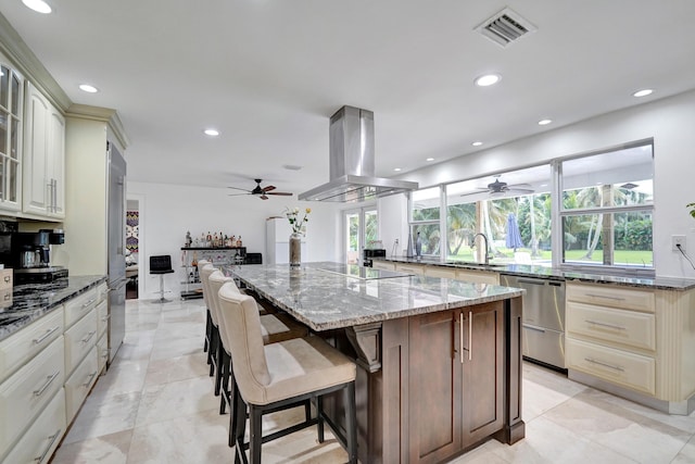 kitchen with island range hood, light stone countertops, a healthy amount of sunlight, and cream cabinets