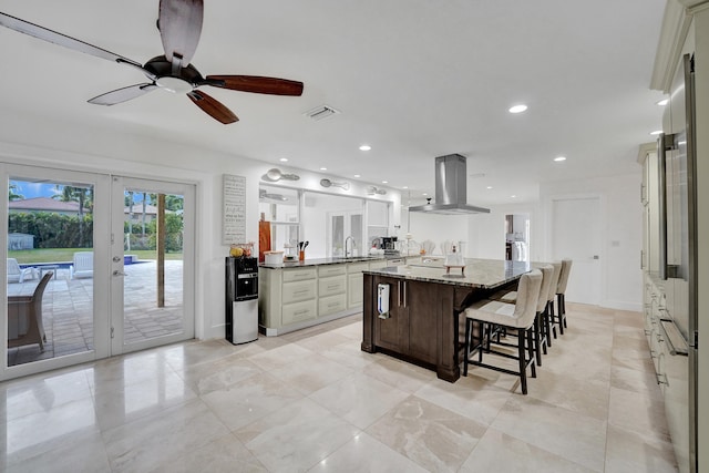 kitchen with island exhaust hood, french doors, light stone countertops, ceiling fan, and a center island