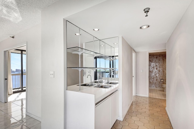 interior space with sink, a water view, light tile patterned flooring, and a textured ceiling