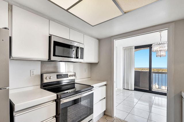 kitchen featuring white cabinets, a water view, light tile patterned floors, appliances with stainless steel finishes, and a notable chandelier