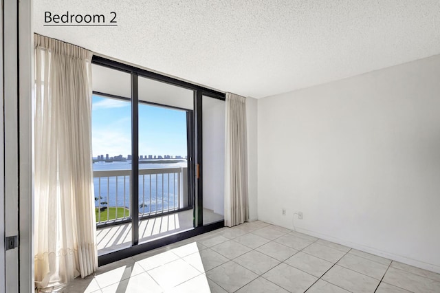 empty room with light tile patterned floors, a textured ceiling, a water view, and a wall of windows